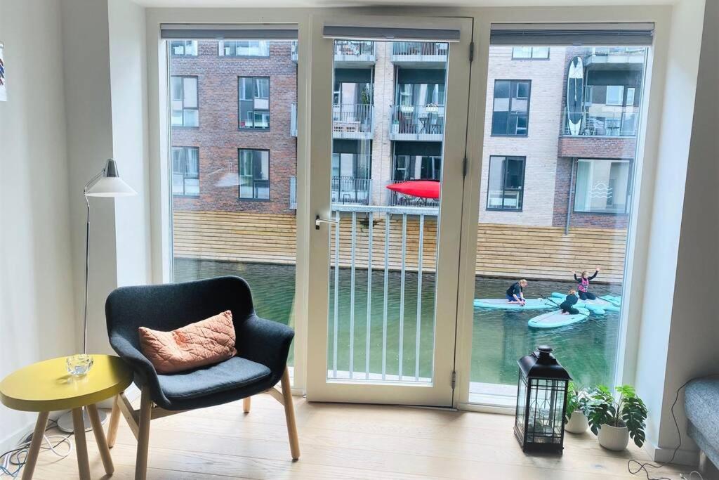 a living room with a sliding glass door with people in the pool at 2Floors New Apartment & Charming Canal Surrounding in Copenhagen