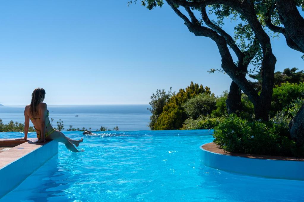 a woman sitting on the edge of a swimming pool at Boutique Hotel Torre Di Cala Piccola in Porto Santo Stefano