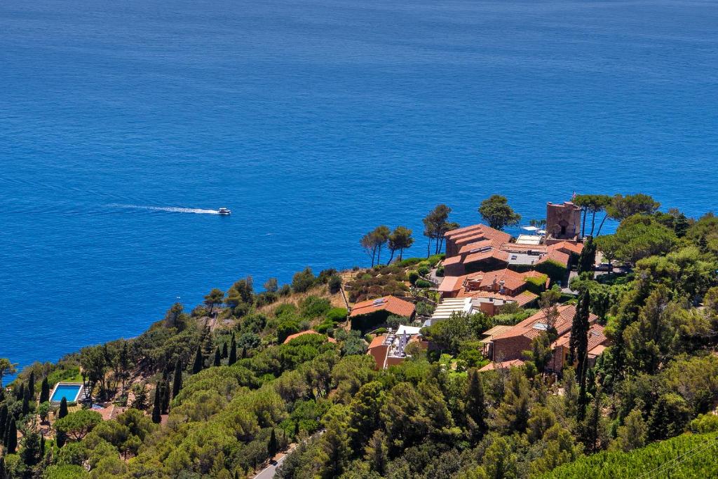 una casa su una collina vicino all'oceano con una barca di Boutique Hotel Torre Di Cala Piccola a Porto Santo Stefano
