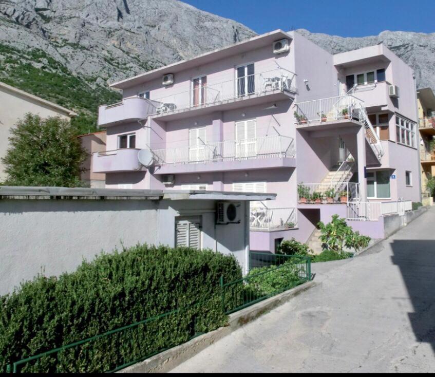 a pink apartment building with a mountain in the background at Apartman Lala in Baška Voda