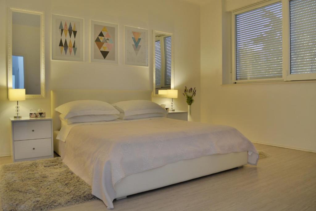 a white bedroom with a bed and two windows at Apartment Seven in Split