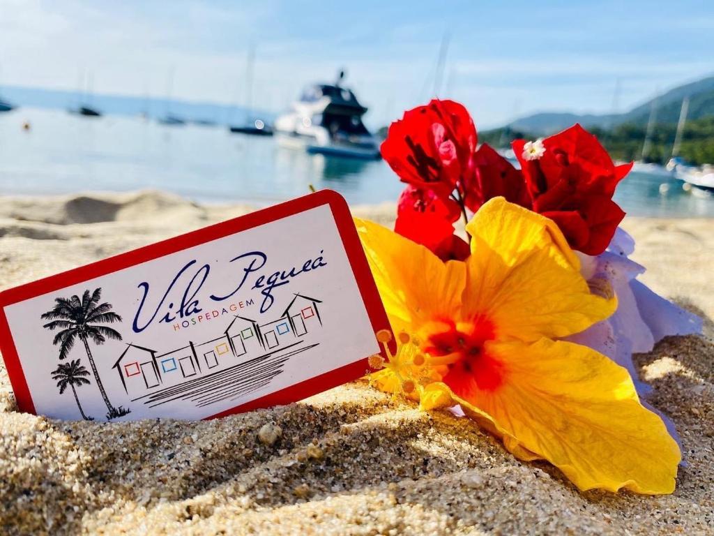 a sign in the sand next to flowers on a beach at Vila Pequeá Ilhabela in Ilhabela