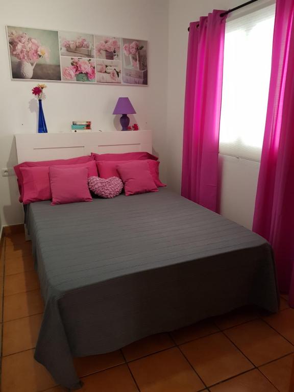 Un dormitorio con una cama con almohadas rosas y una ventana en Casa Dulce, en Gran Tarajal