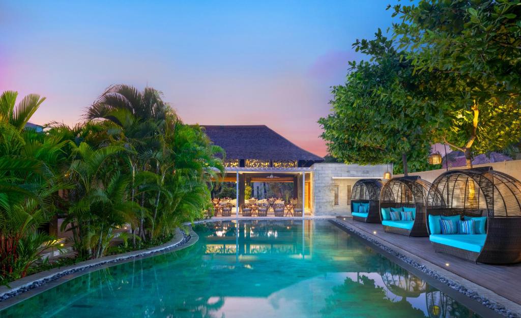 Avani Seminyak Bali Resort في سمينياك: مسبح والكراسي الزرقاء بجانب المنزل