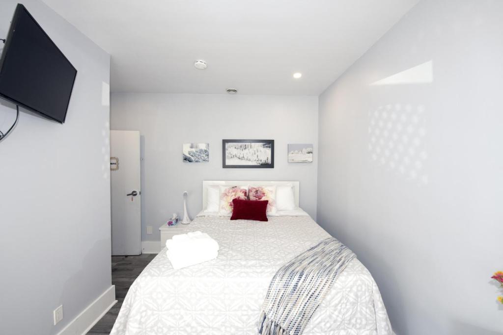 a white bedroom with a white bed with a red pillow at Serene Niagara Inn in Niagara Falls