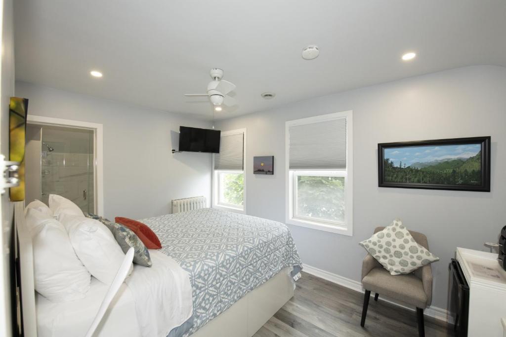 a white bedroom with a bed and a chair at Serene Niagara Inn in Niagara Falls