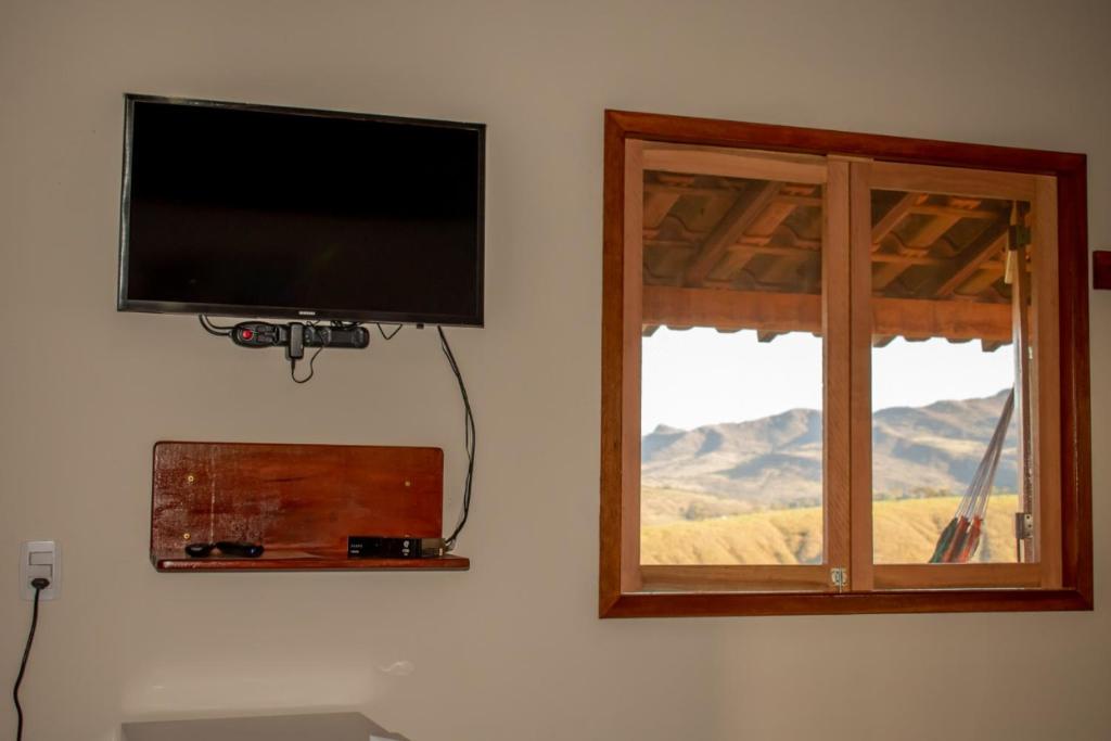 uma televisão de ecrã plano numa parede ao lado de uma janela em Refúgio Pé da Serra - Chalés em São Roque de Minas