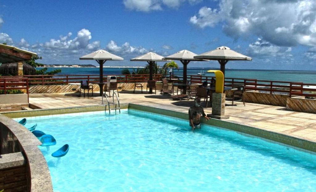 a swimming pool with tables and umbrellas and the ocean at Pipa´s Ocean Flat in Pipa