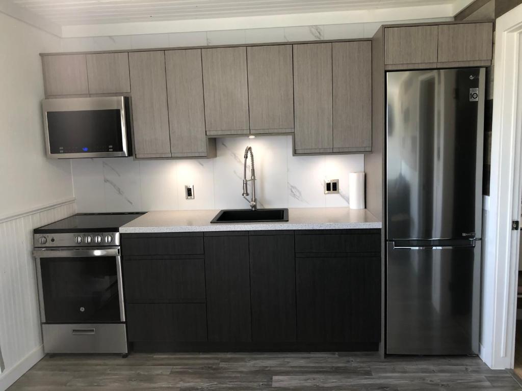a kitchen with black cabinets and a stainless steel refrigerator at Newly Renovated Confederation Bridge View Cottages in Borden