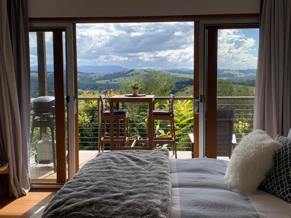 a bedroom with a bed and a balcony with a view at Callemondah Studio with stunning views, in Bangalow and Byron Hinterland in Bangalow