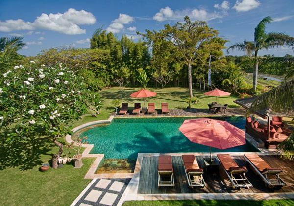 a swimming pool with chairs and umbrellas in a yard at Anyar Estate in Canggu