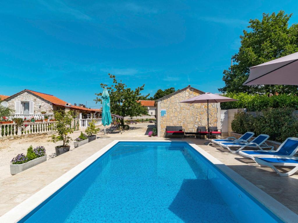 a pool with chairs and umbrellas next to a house at Holiday Home Glavica by Interhome in Medaki
