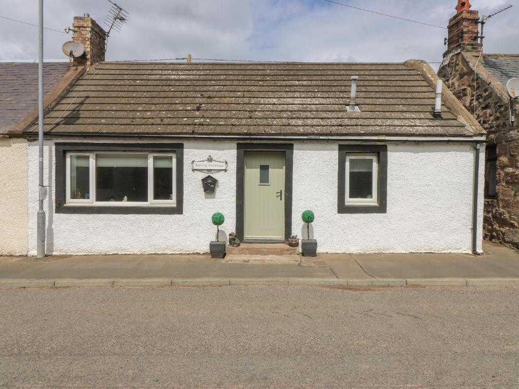 a white house with a green door on a street at Spring Cottage in Duns