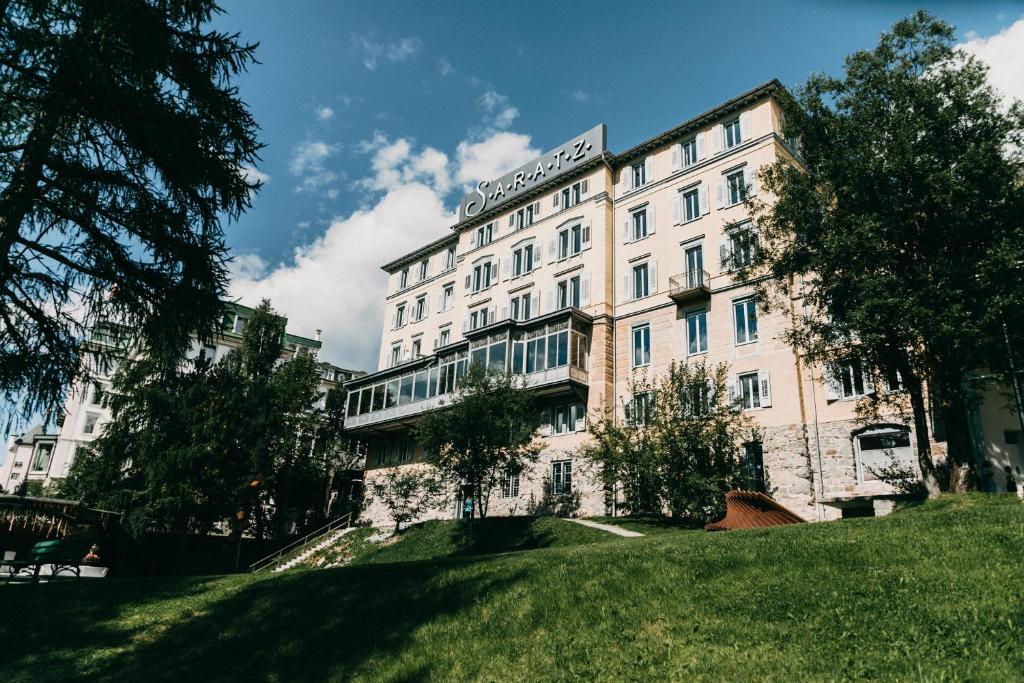 een groot wit gebouw op een grasheuvel bij Hotel Saratz Pontresina in Pontresina