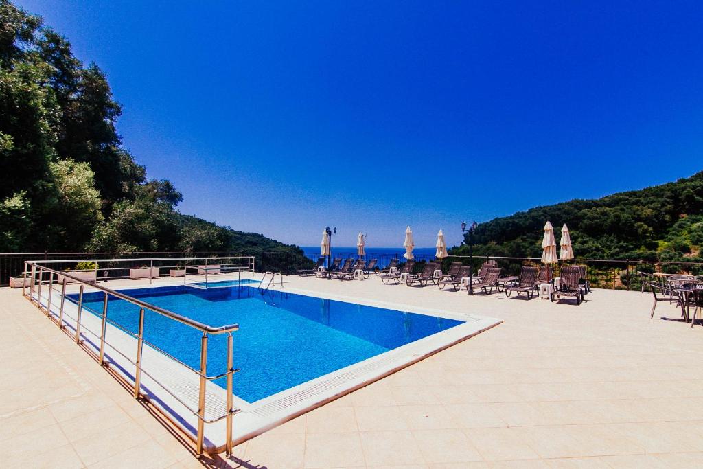 a swimming pool with chairs and umbrellas and the ocean at Petrino Apartments in Parga