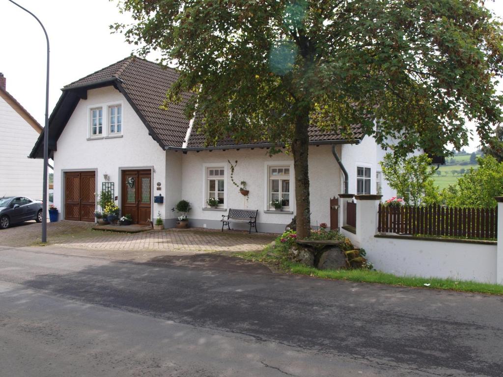 Una casa blanca con un árbol delante. en Ferienwohnung Zauberhaft, en Schalkenmehren