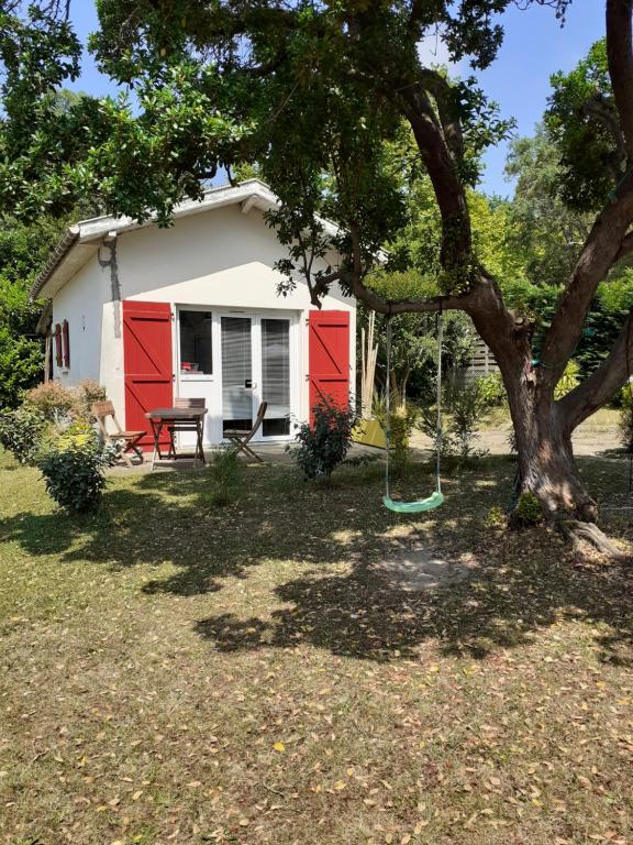une maison rouge et blanche avec un arbre et une balançoire dans l'établissement Maisonnette proche de la plage, à Tarnos
