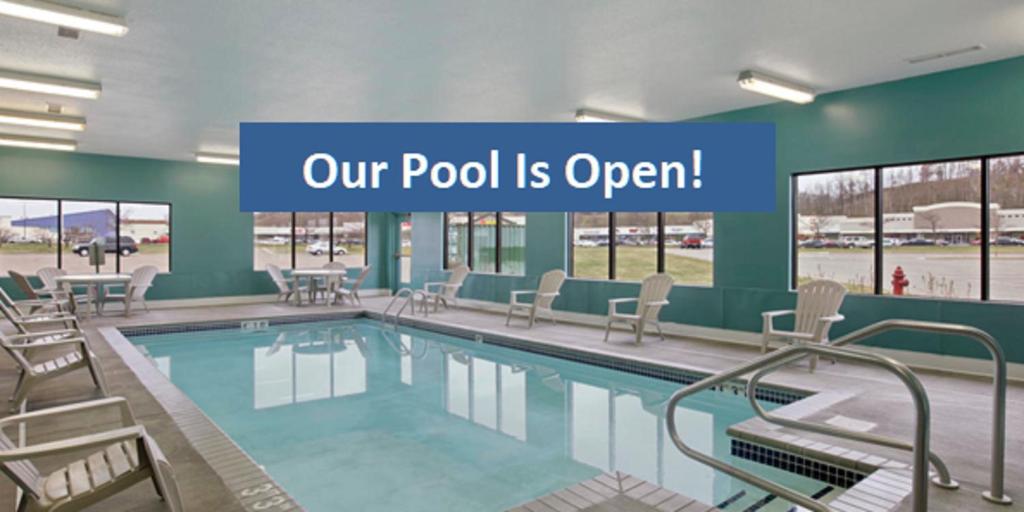 a pool with chairs and a sign that reads our pool is open at Baymont by Wyndham Eau Claire WI in Eau Claire