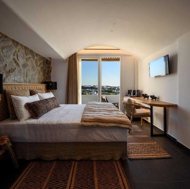 Vrachos Suites Mykonos في مدينة ميكونوس: غرفه فندقيه بسرير ومكتب ونافذه