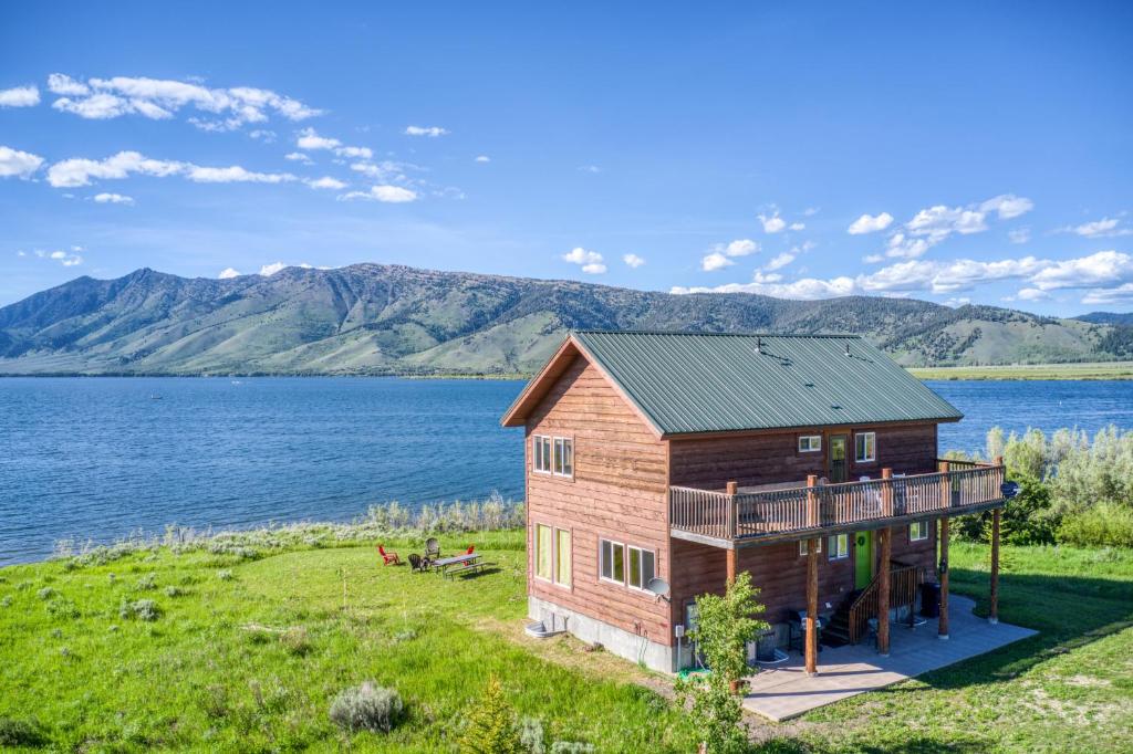 a house on the lake with mountains in the background at Henrys Lake Goose Bay by KABINO On Henrys Lake almost 3 Acres Satellite Wifi in Island Park