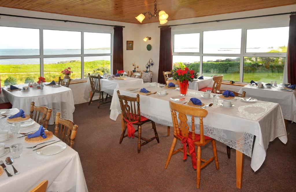una sala da pranzo con tavoli e sedie bianchi e finestre di The Olde Castle B&B a Renvyle
