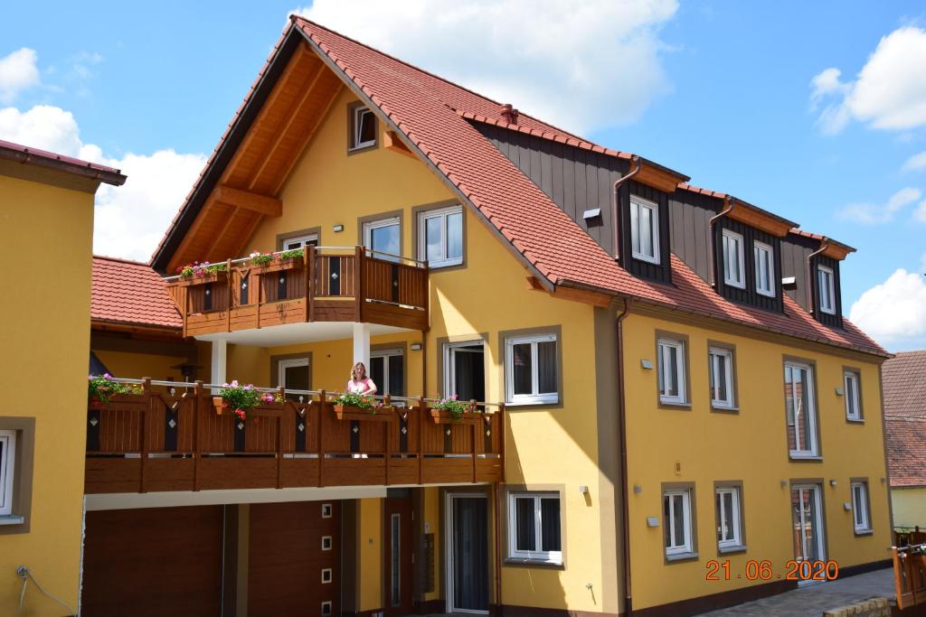 a yellow building with a balcony and a woman sitting on a porch at Ferienwohnungen Fewo Landglück in Herrieden