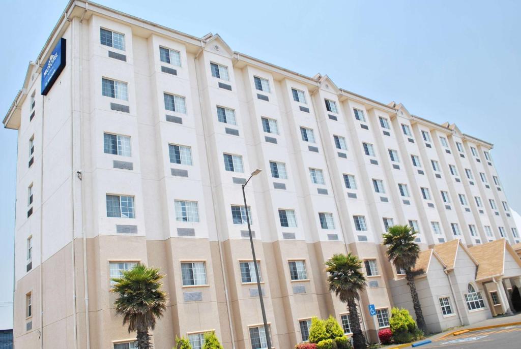 a large white building with palm trees in front of it at Microtel Inn and Suites by Wyndham Toluca in Toluca