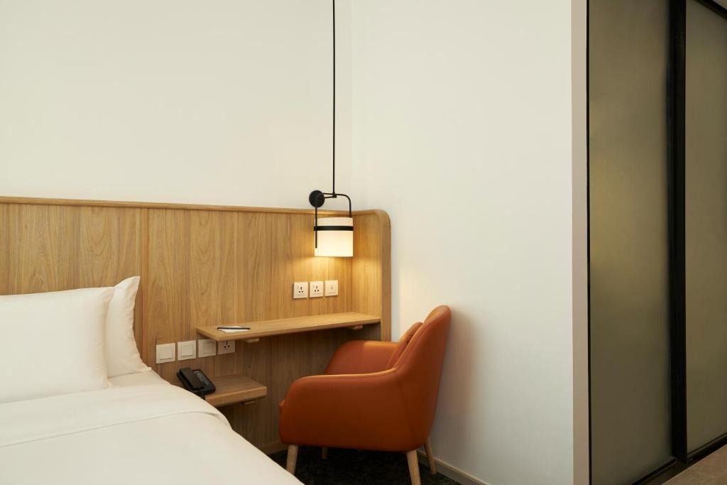 A small wall-mounted desk and orange armchair occupy the corner beside the bed.