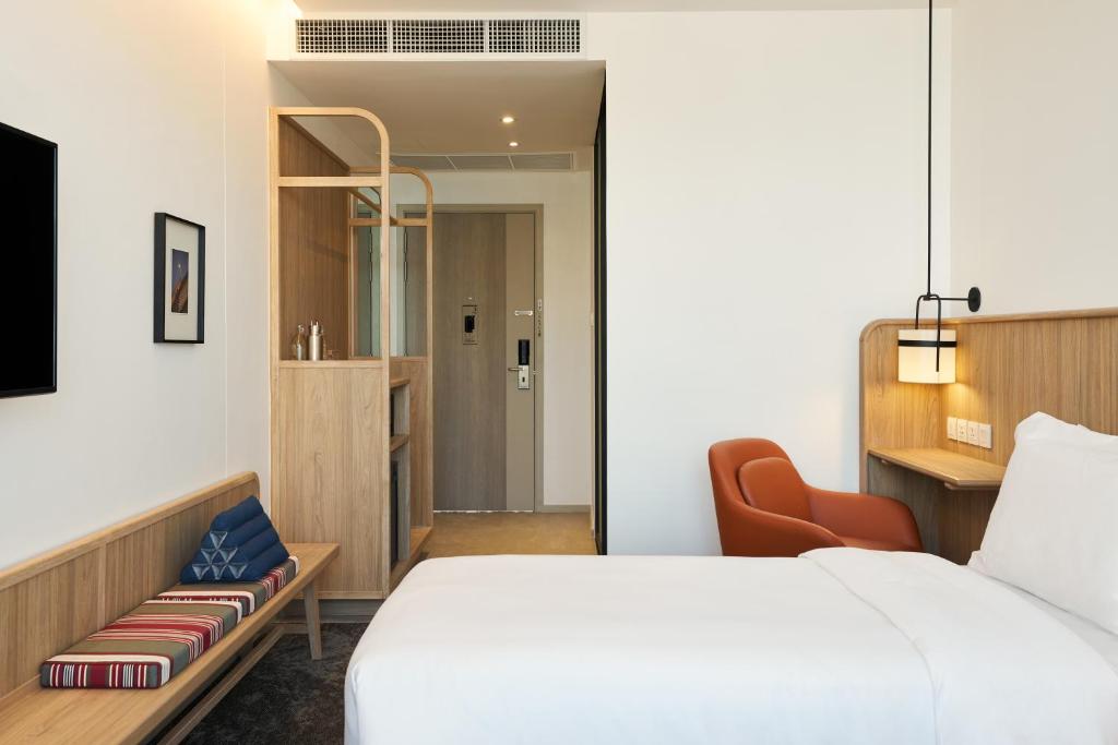 A guest room with a large bed, orange chair, built-in desk, and open storage.
