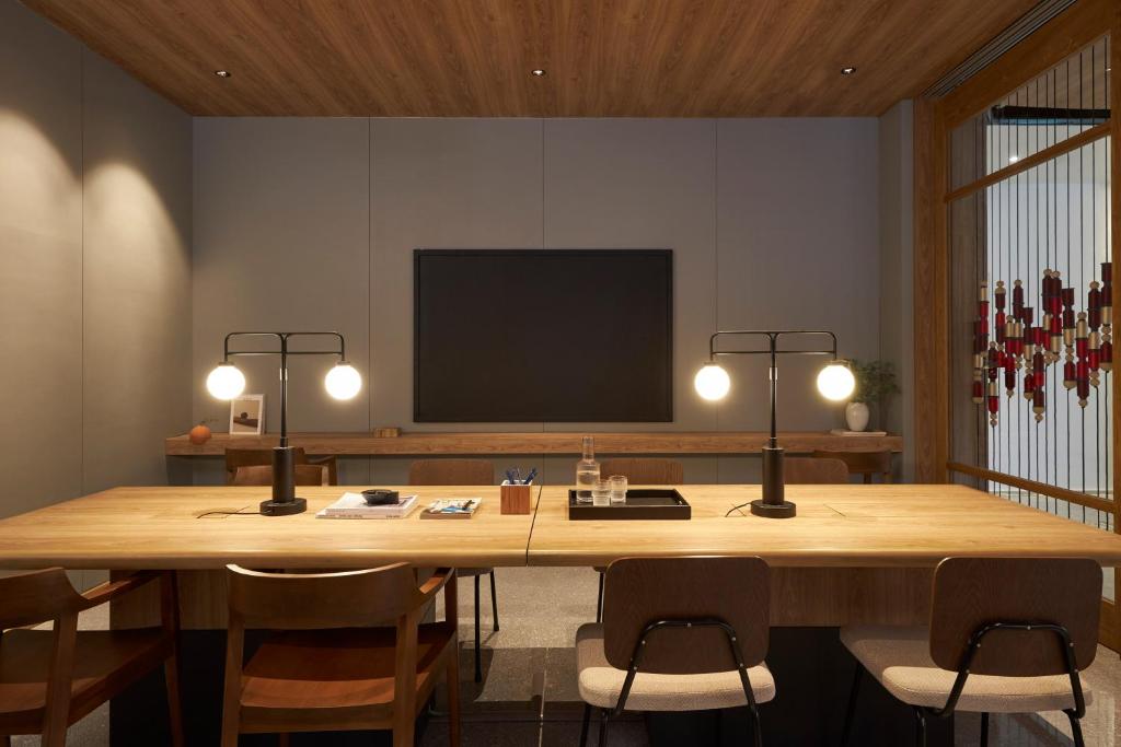 A warmly lit conference room with a long wooden meeting table and wall-mounted screen.
