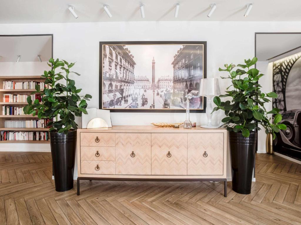 a living room with a dresser and two plants at Hotel Royal Saint Honore Paris Louvre in Paris