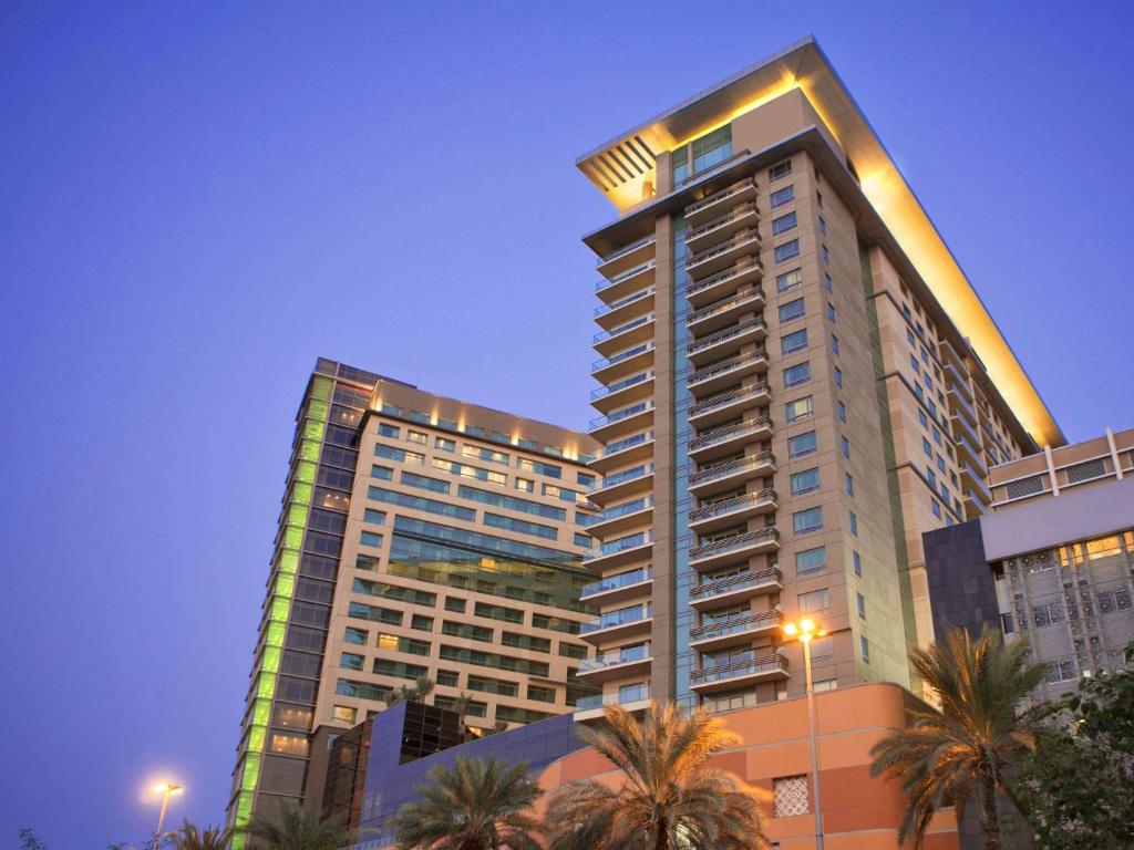 a tall building with palm trees in front of it at Swissôtel Living Al Ghurair in Dubai