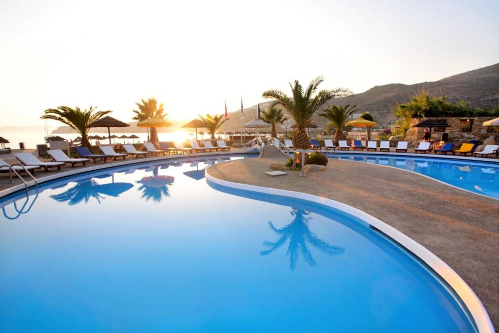uma piscina num resort com cadeiras e palmeiras em Far Out Village Hotel em Mylopotas