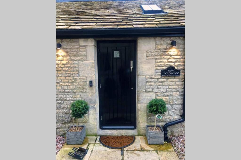 a black door on a stone house with two plants at New Loos Cottage, Old School Court in Stow on the Wold