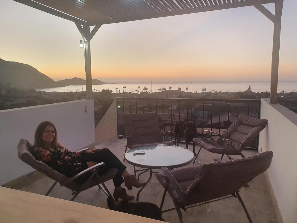 a woman sitting on a balcony with a table and a dog at Hosteria Piedra Blanca in Taltal