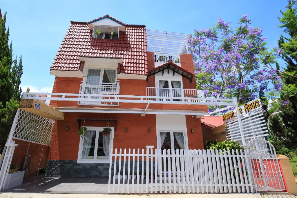 ein rotes Backsteinhaus mit einem weißen Zaun in der Unterkunft Maison de Fleurs - Ngôi Nhà Hoa in Da Lat