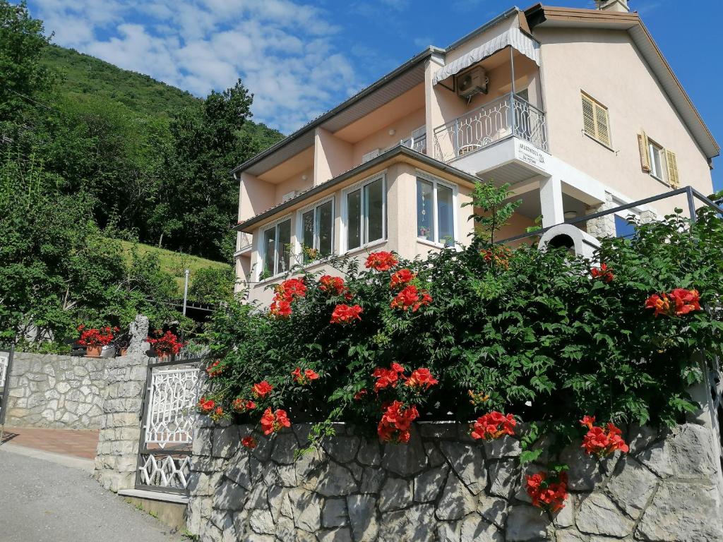 a house with red flowers on a stone wall at Apartments Tonka in Mošćenička Draga