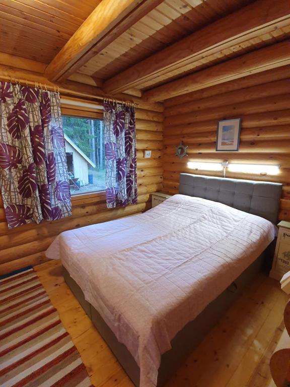 a large bed in a wooden room with a window at Viihtyisä hirsimökki järven rannalla in Siikainen