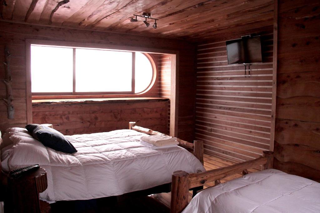 a bedroom with two beds and a window and a tv at Hotel Mitos in Quellón