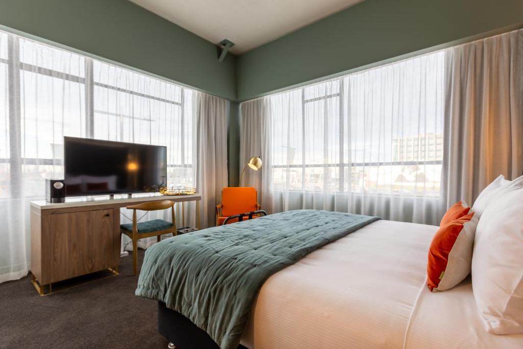 um quarto com uma cama e uma secretária com uma televisão em The Muse Christchurch Art Hotel em Christchurch