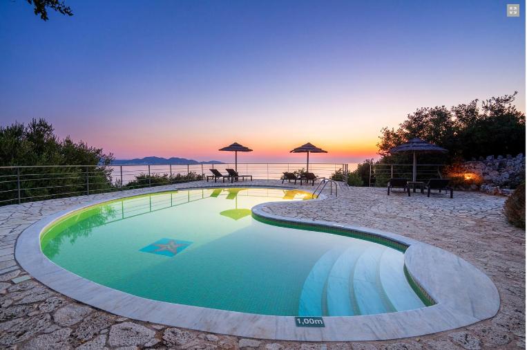 a swimming pool on the beach with a sunset in the background at Stone Cottages in Khalikerí