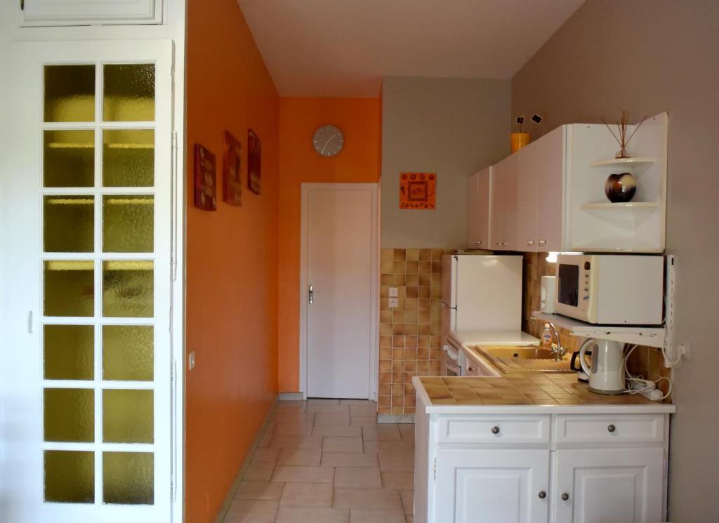 een keuken met witte kasten en een oranje muur bij APPARTEMENTS DANS VILLA EN REZ DE JARDIN in Hyères
