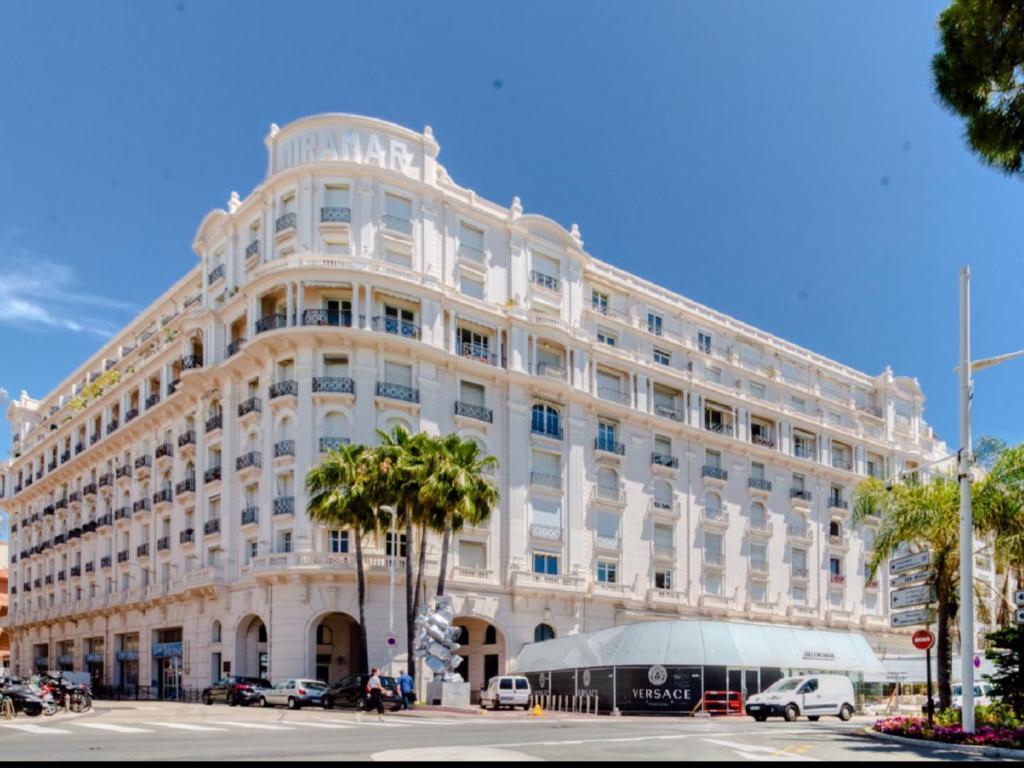 un grand bâtiment blanc avec des palmiers devant dans l'établissement Cannes Croisette Majestic Miramar, à Cannes