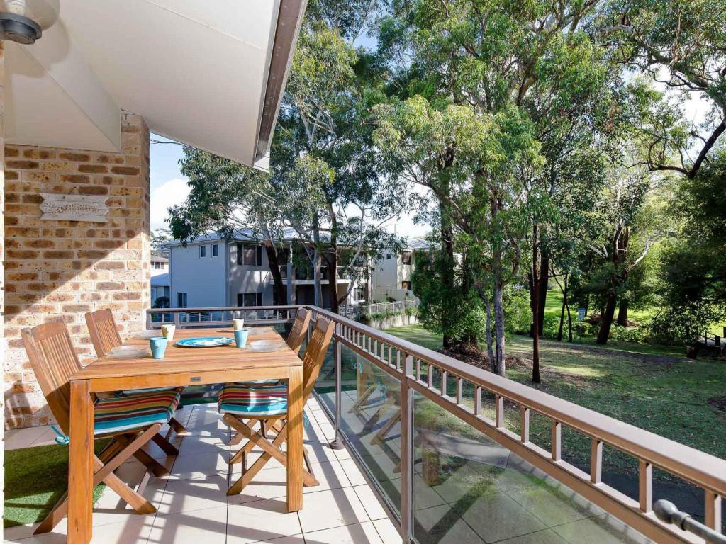 un patio con tavolo e sedie in legno su un balcone di Bay Parklands, 54 2 Gowrie Avenue - air con, wifi, pool, tennis court,child friendly a Nelson Bay