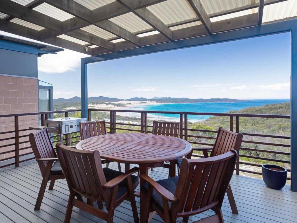 une table et des chaises en bois sur une terrasse avec vue dans l'établissement Beach House 7 26 One Mile Close air conditioned wifi foxtel linen, à Anna Bay