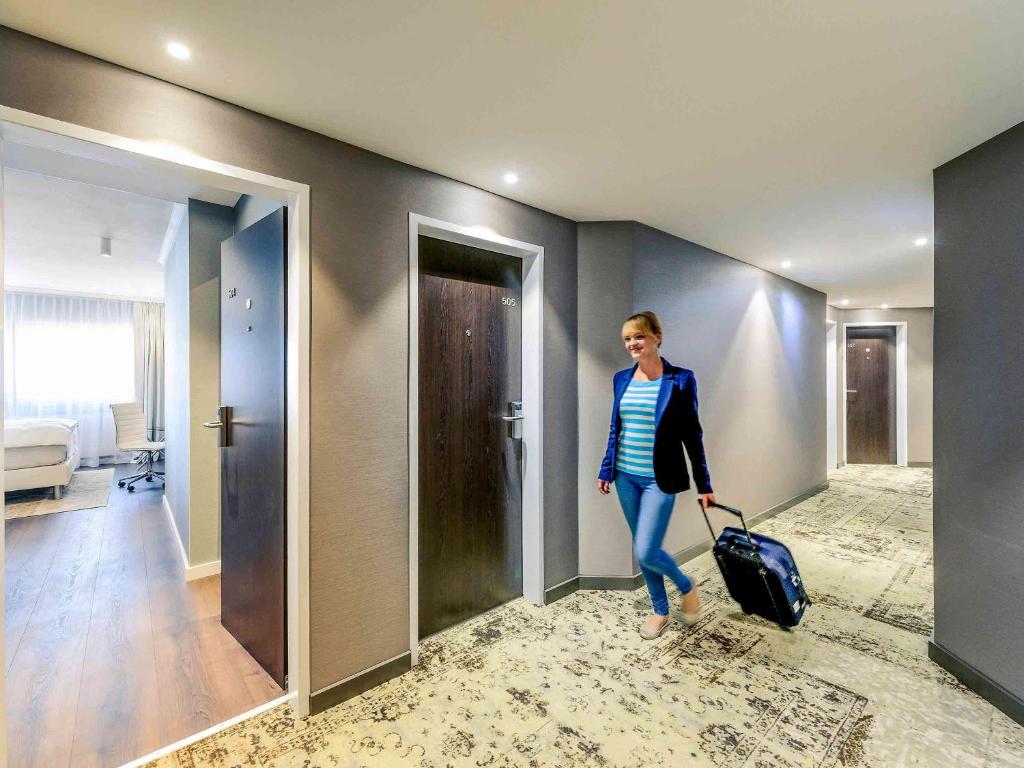 une femme traversant un couloir avec une valise dans l'établissement Mercure Hotel Raphael Wien, à Vienne