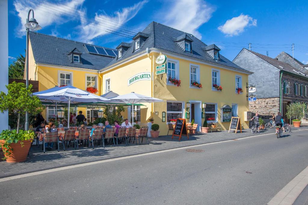 un grupo de personas sentadas en mesas frente a un edificio amarillo en Hotel zur Post en Mülheim an der Mosel