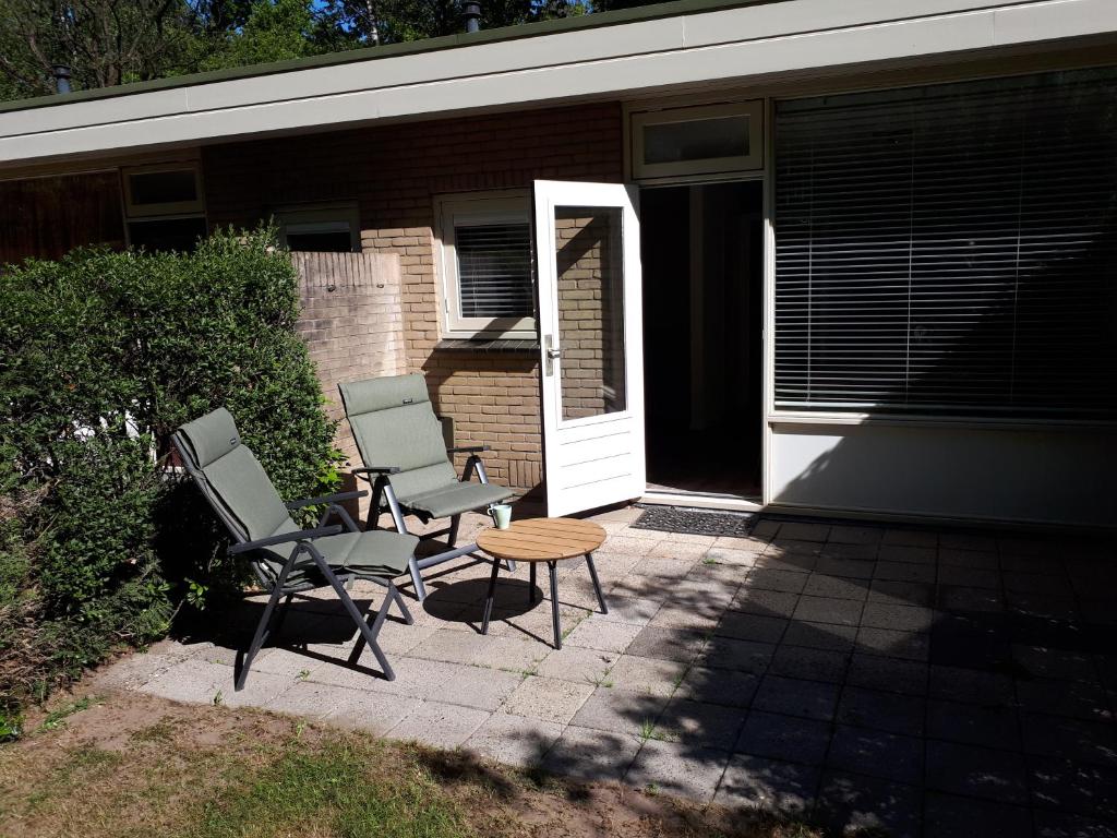 two chairs and a table in front of a house at Huisje Koolmees park Hoefbos Otterlo in Otterlo
