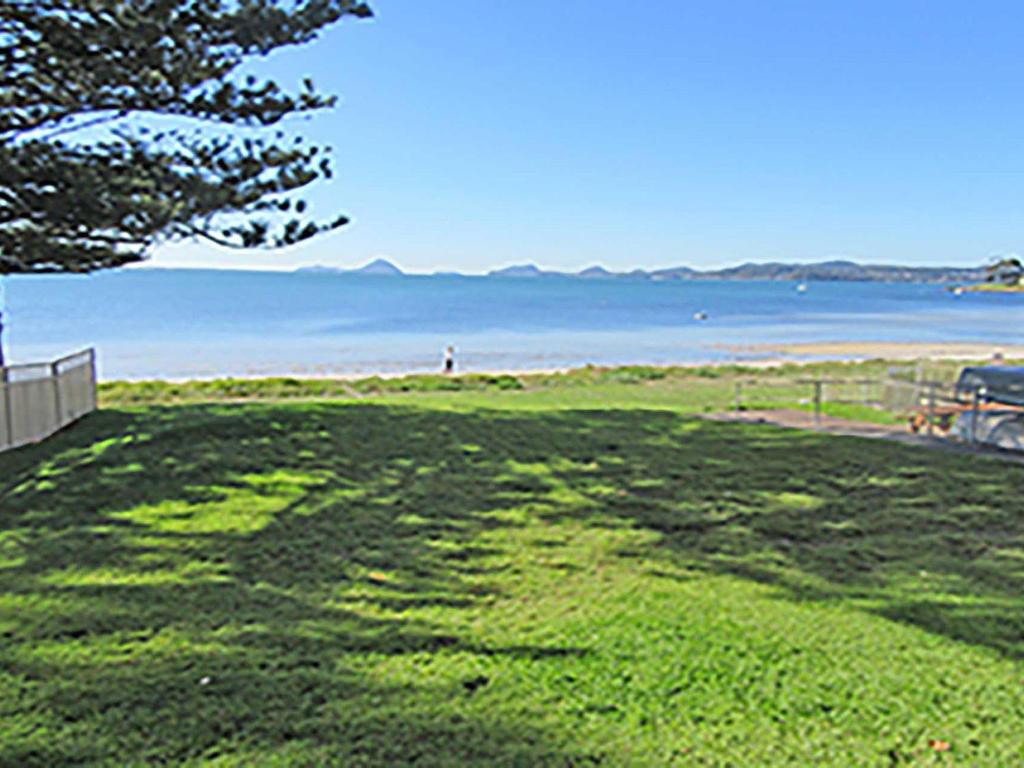 a grassy field with a person standing on the beach at 15 'Kanangra', 39 Soldiers Point Road - fantastic unit right on the water in Soldiers Point