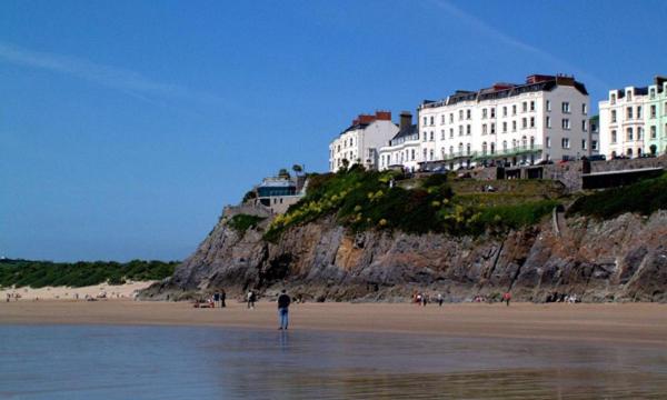a person standing in the water on a beach with buildings at Carnock in Tenby
